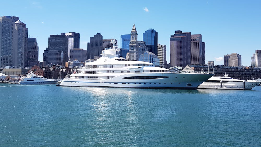 A large yacht docked in a body of water with a city in the background.