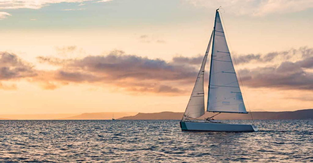 A sailboat gracefully glides across the ocean at sunset.