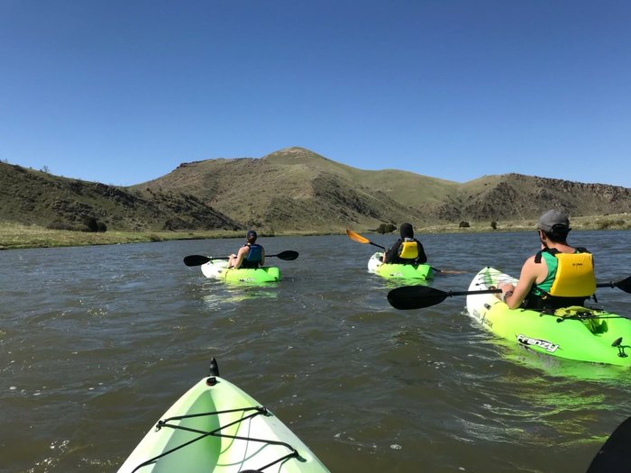 Three kayakers paddling on America’s river with mountains in the background.
