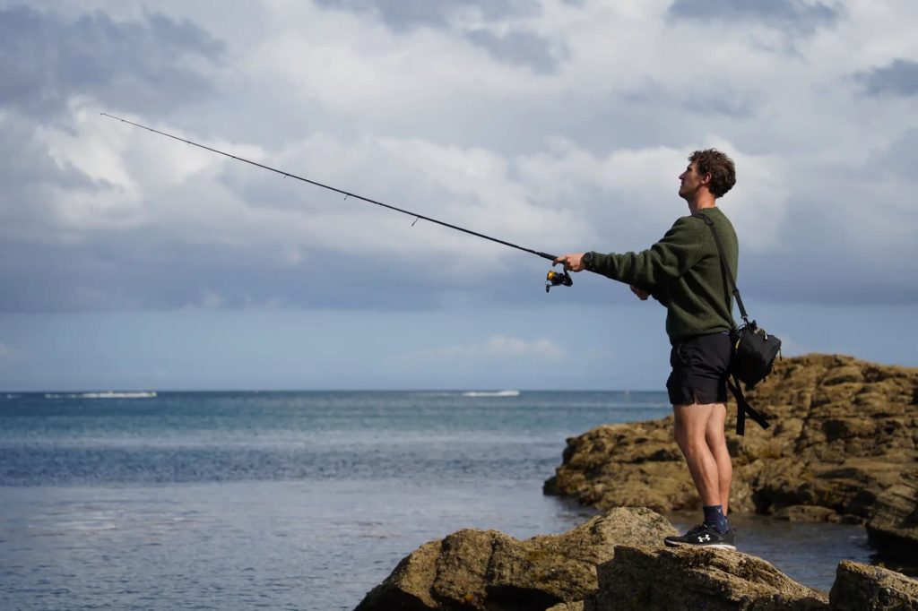 A man is fishing on rocks near the ocean.